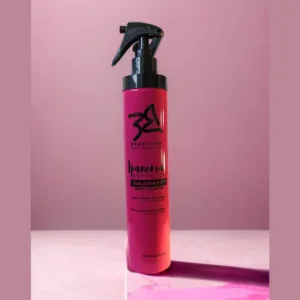 La imagen muestra un envase plástico color fucsia con bomba spray color negro que es un protector térmico para el cabello.