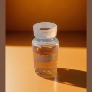 La imagen muestra un frasco pequeño con un líquido color amarillo que contiene keratina líquida ampolla, sobre una mesa.